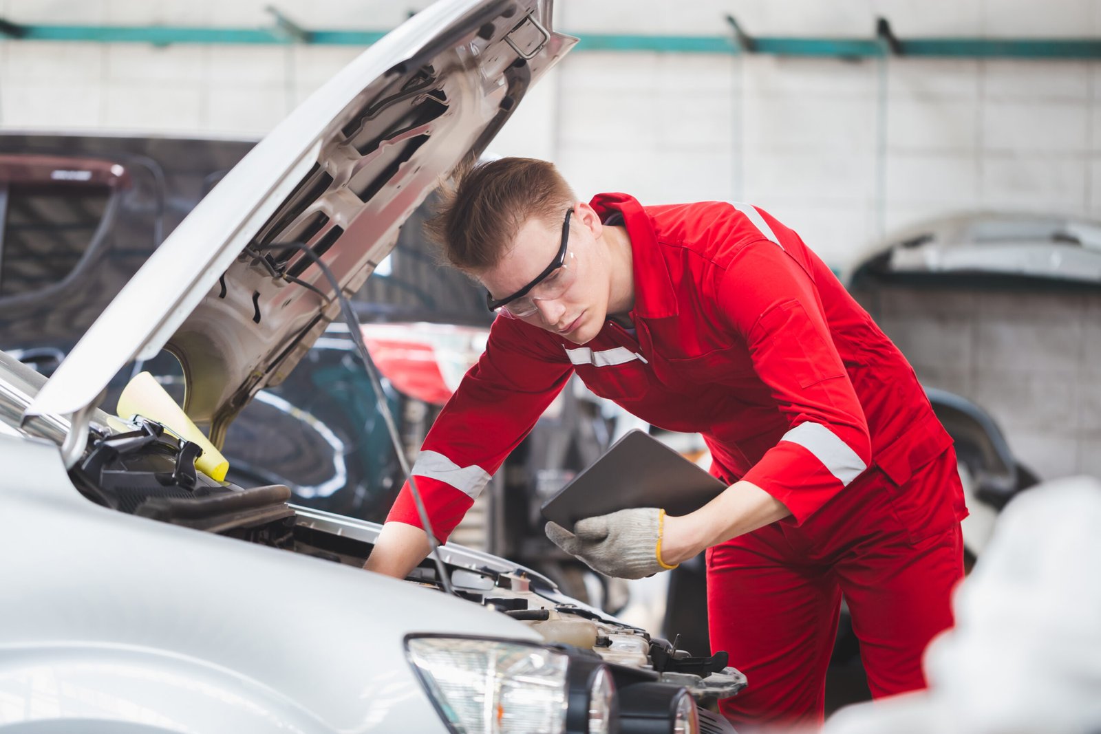 Caucasian car mechanic with tablet standing by vehicle engine area with hood open technician checking modern car garage car repair maintenance concepts scaled